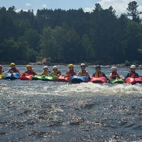 Group of kayakers in colorful kayaks on a river with forested background.