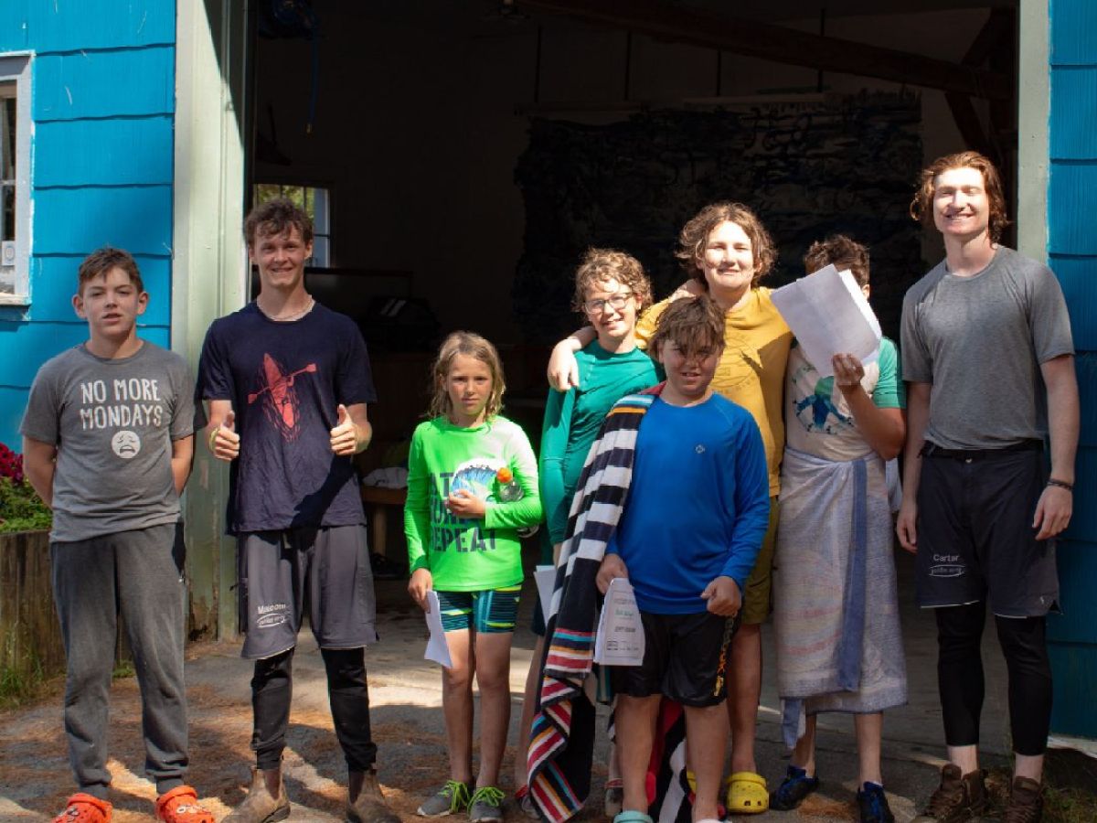 Group of kids and adults posing outside a blue building in casual clothes.