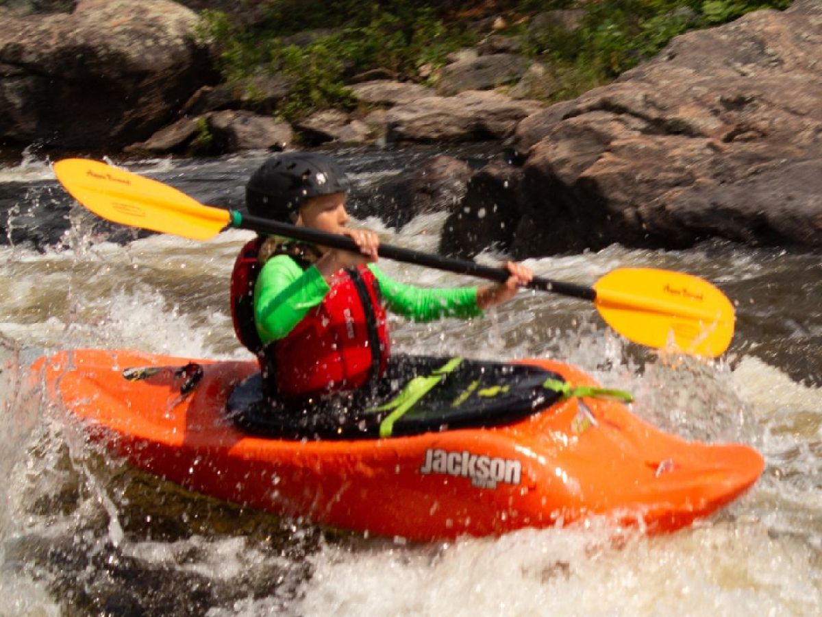 Person kayaking in rapid water with orange kayak and yellow paddle.