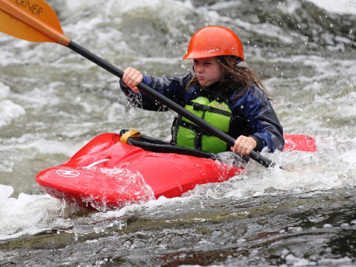 Person kayaking in rough waters wearing a helmet and life jacket.
