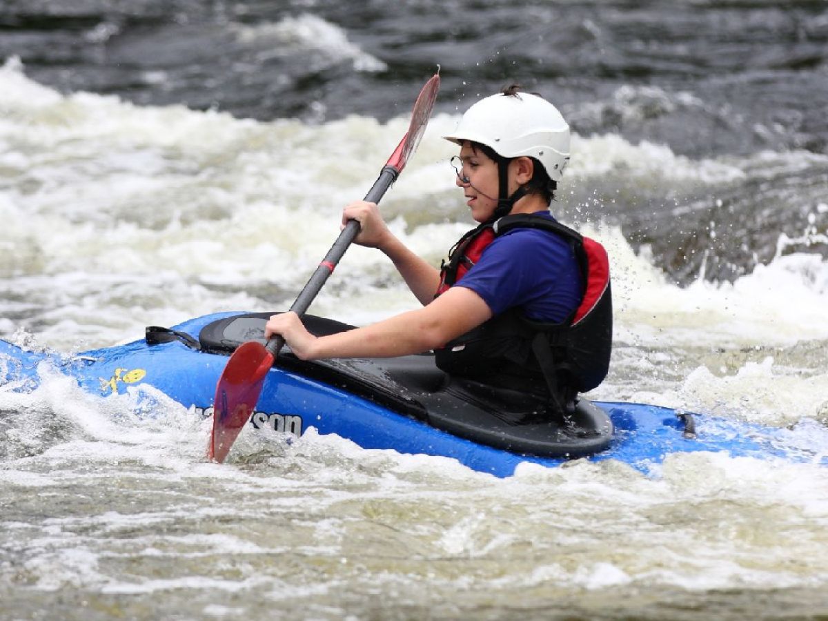 Person in helmet kayaking through rapids on a river.