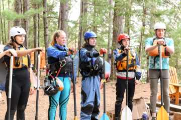 5 people listening to instructions outside in kayaking gear