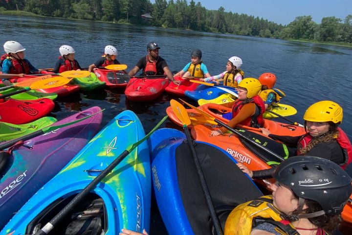 Group of kayakers in colorful kayaks gathered on a lake, wearing helmets and life vests.