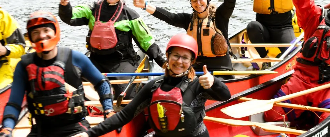 Group of people smiling and giving thumbs up while sitting in canoes on a river.