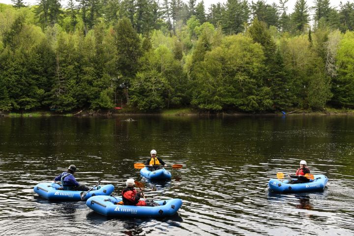 Four people in blue inflatable kayaks on a forest-surrounded lake.