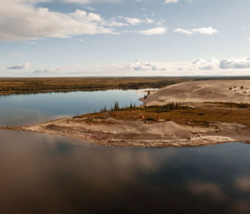 Aerial view of a calm, reflective lake with a sandy shore and sparse vegetation.