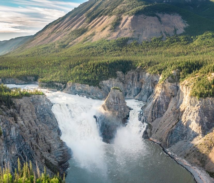 Aerial view of a large waterfall cascading between rocky cliffs and surrounded by forested mountains.