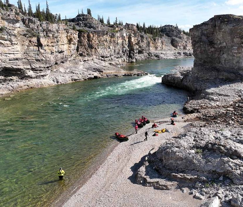 Canoers on a rocky riverbank in a canyon with clear water and stone cliffs.