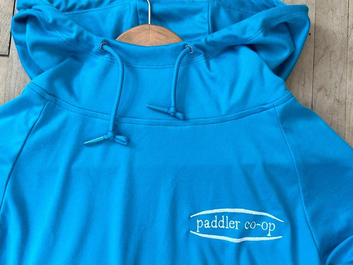 Blue hoodie with 'paddler co-op' logo on wooden hanger.