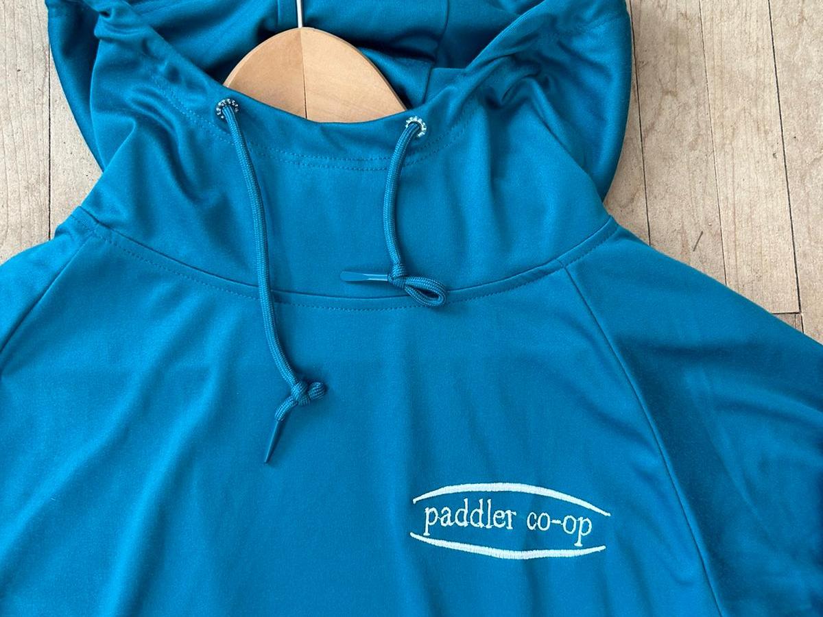 Blue hoodie with paddler co-op logo on wood hanger.