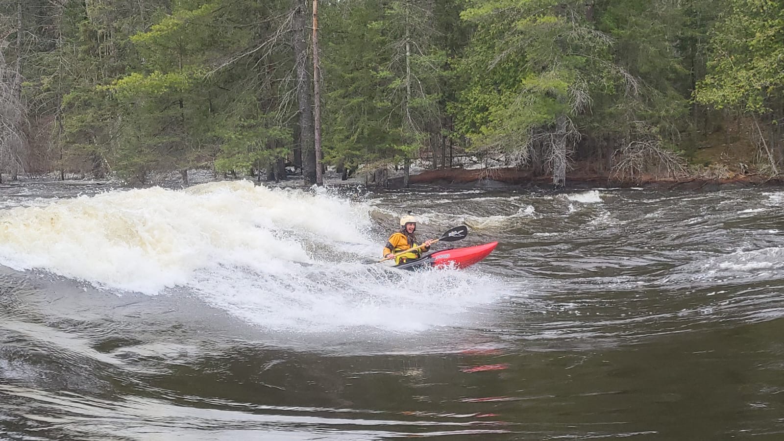 Person in a kayak navigating river rapids with trees in the background.