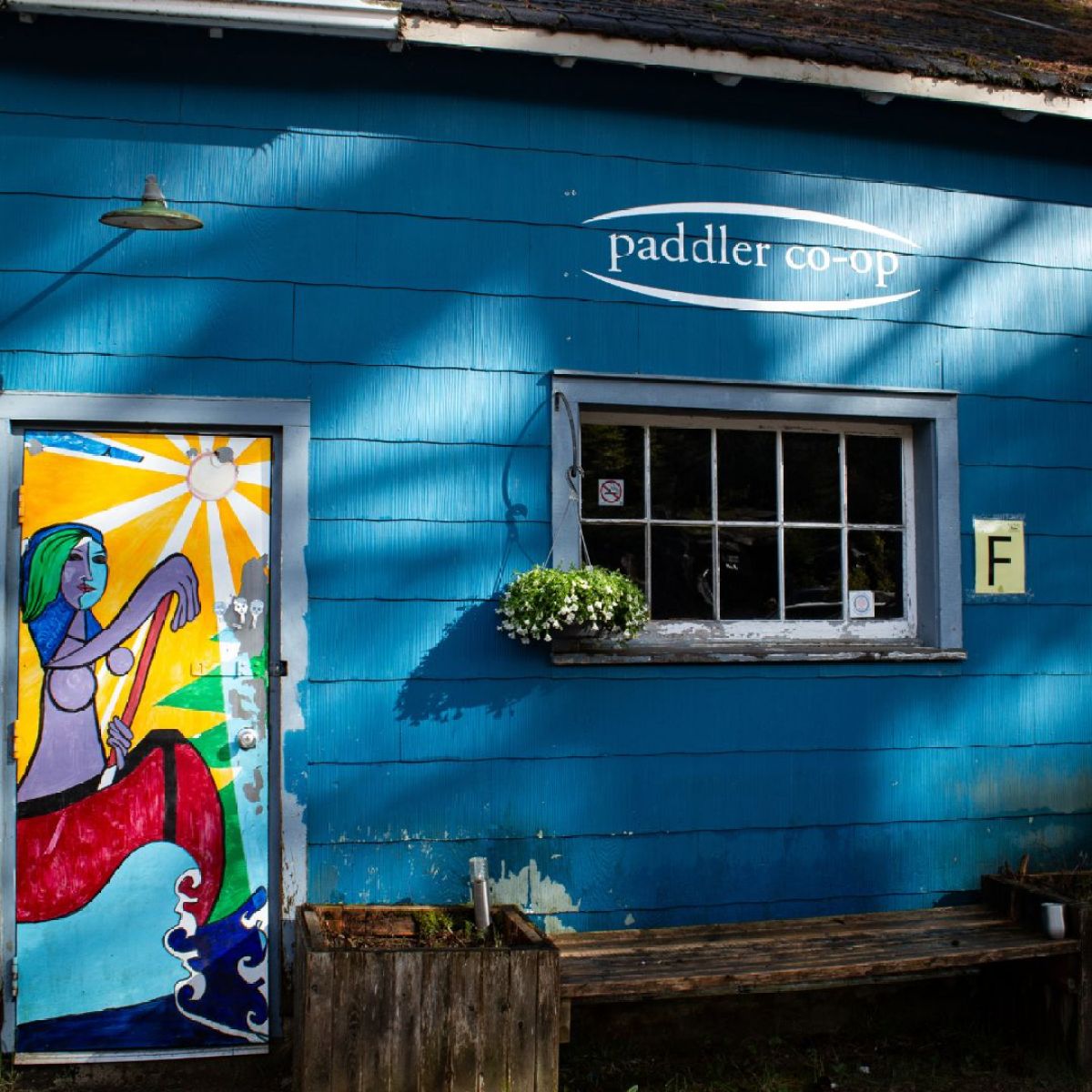 Blue building with a colorful mural on the door depicting a person paddling on water.
