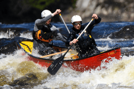 Two people in helmets canoeing through rapids.